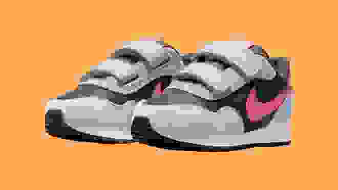Black, white and pink Nike MD Valiant sneakers in front of orange background.