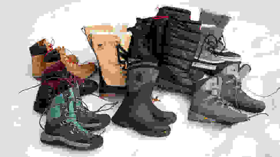 A number of pairs of winter boots, from various brands, laid out on a bed of snow.
