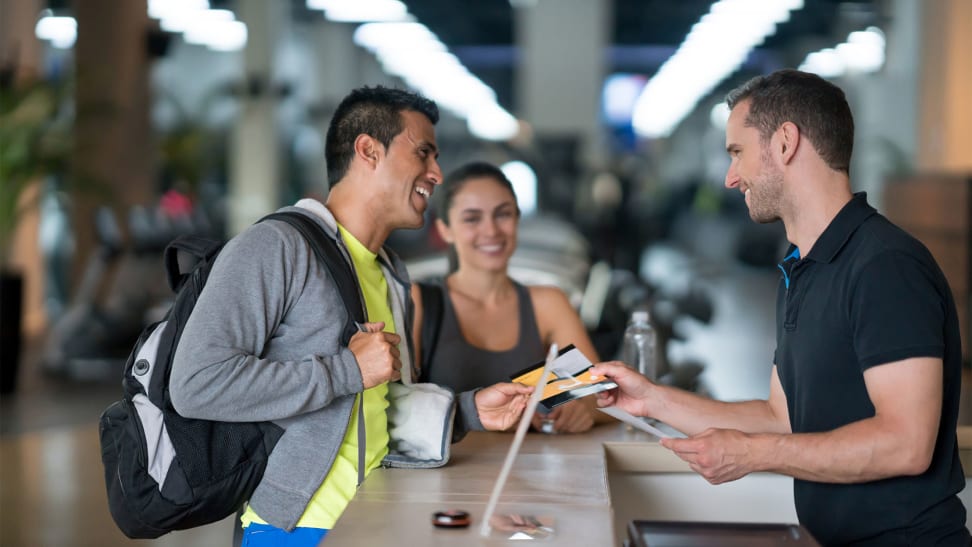 A man and a woman talking to a gym employee at the front desk.