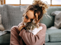 Young woman hugging her cat in front of couch