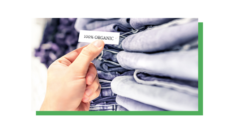 Stacks of jeans folded on a shelf, with a hand holding a tag that reads "100% organic."