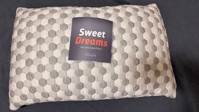 White and grey hive pattern of the Layla Sleep Kapok Pillow with "sweet dreams" packaging card on top, against a dark grey background.