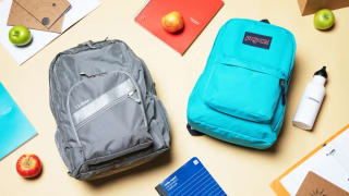 Gray backpack next to blue backpack surrounded by school supplies