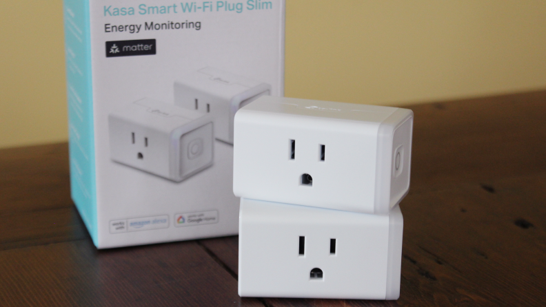 Kasa Smart Wi-Fi plugs stacked on top of each other, next to a box of Kasa Smart Wi-Fi plugs.