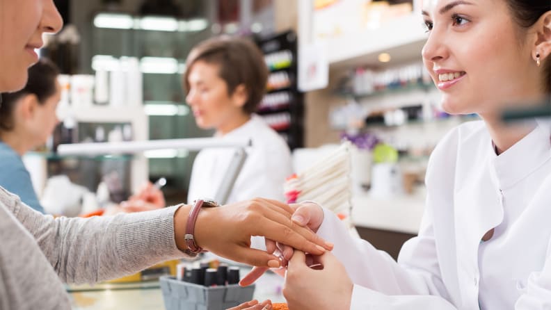 A nail tech holding their client's hand while talking to them.