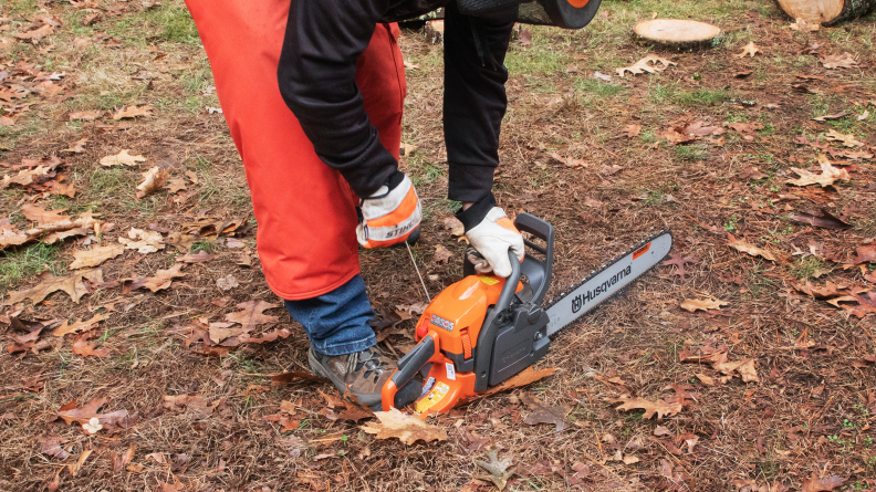 A person outdoors wearing safety gloves while holding a chainsaw