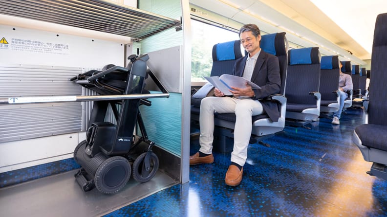 A person rides a train with their wheelchair folded on the side.