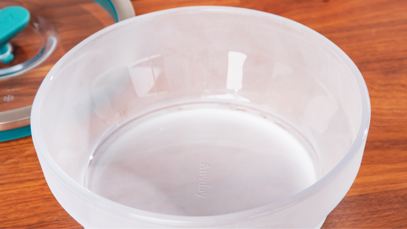 Clear microwavable bowl with lid removed on top of wooden countertop.