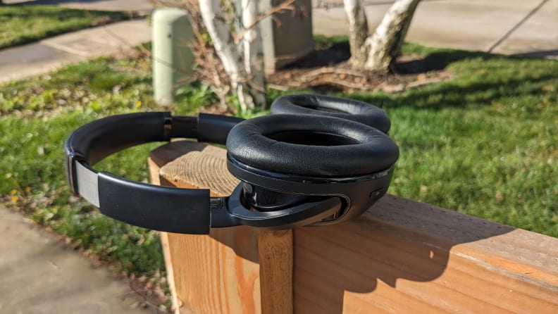 The JBL Tour One M2 headphones sitting face up on top of a wooden post on a sunny day.