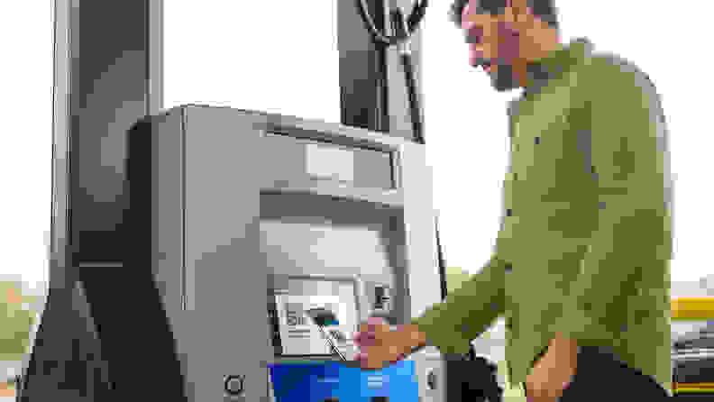 A person shown standing by a gas pump paying for gas with their smart phone.