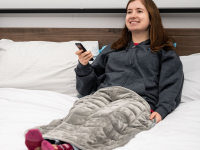 女人躺在床上拿着遥控器，灰色的毯子盖在她的腿上
