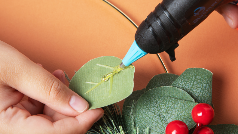 A person hot gluing onto a fake floral leaf.