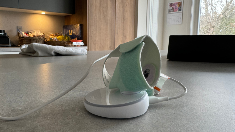 A mint green Owlet Dream Sock sitting on a charging doc on a marble countertop in kitchen.
