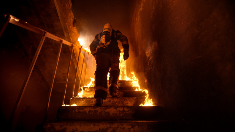 Firefighter walking up stairs in fire-filled home.