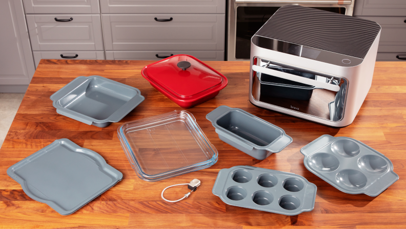 The Brava Glass Oven on a wooden countertop next to assorted cooking trays and dishes.