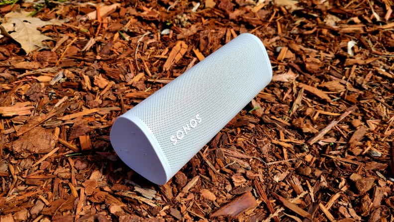 The tubular and white Sonos Roam sits on a bed of red bark