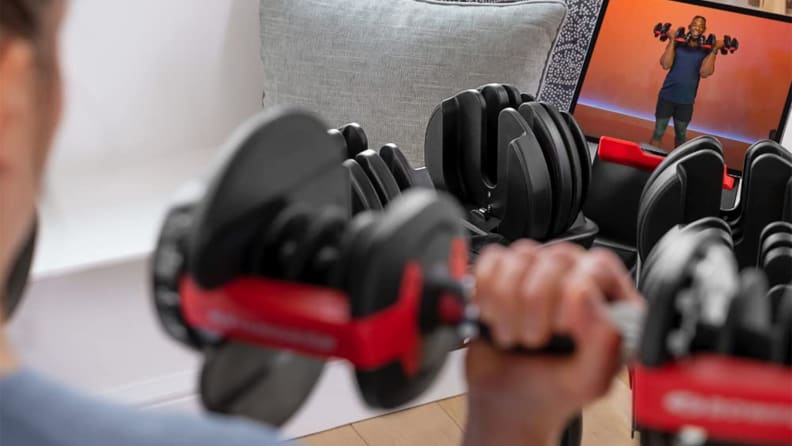 A person using the Bowflex adjustable dumbbells while watching a workout video.