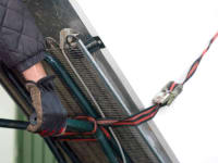 A person with work gloves is moving an old refrigerator secured to a dolly.