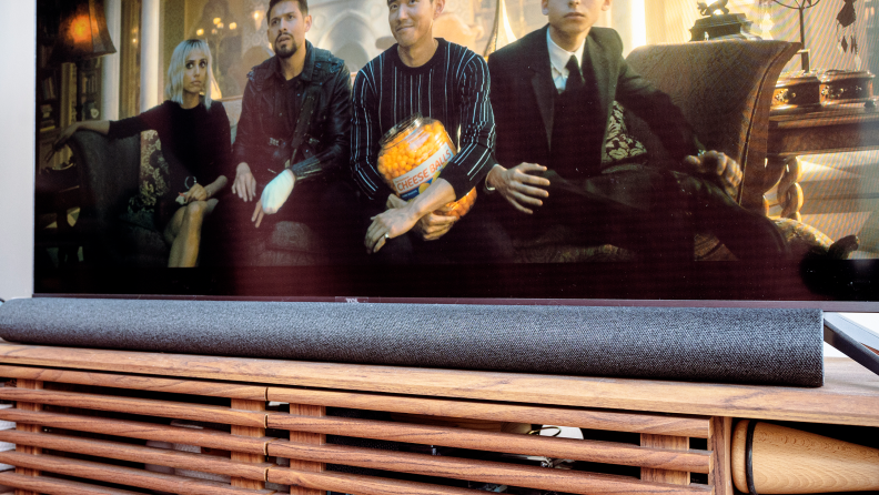 A black soundbar sits on a wooden TV console under a TV with Umbrella Academy playing.