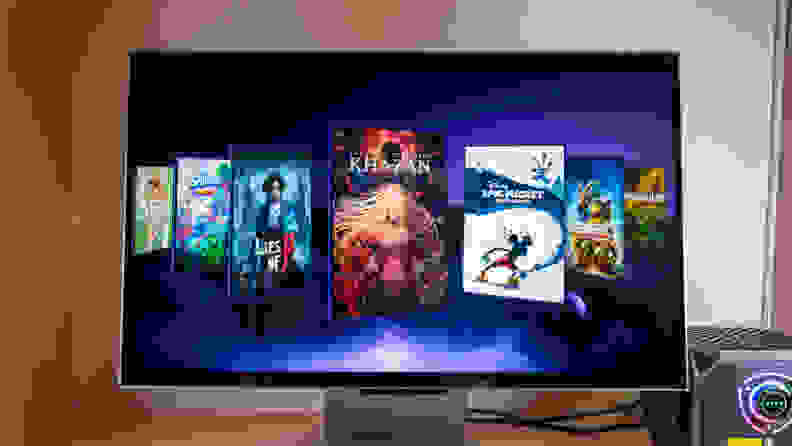 A large 3D gaming monitor sits on a desk with a gallery of video games on its screen