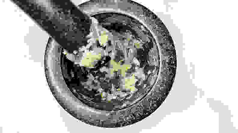 A person grinds alliums into a pulp using a mortar and pestle.