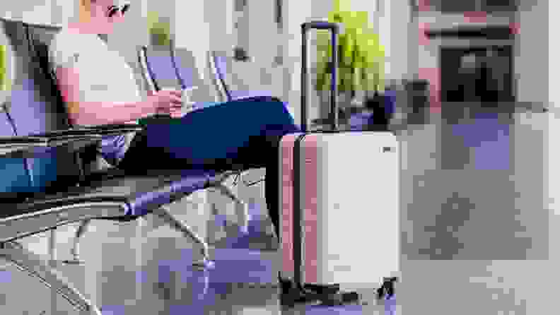 Person sitting in airport terminal next to suitcase