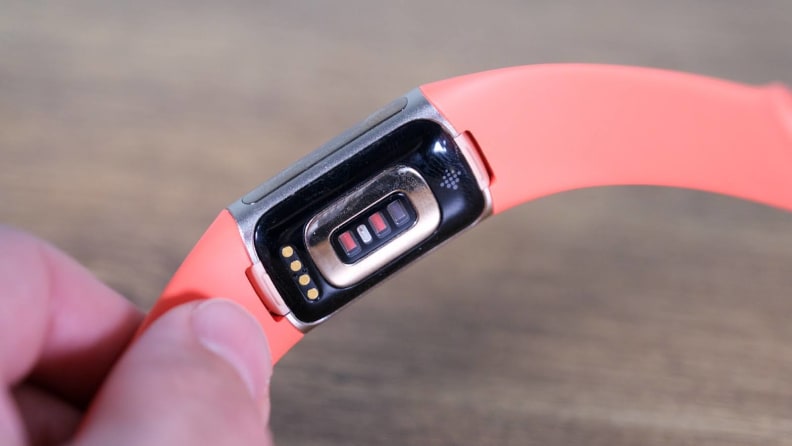 Person holding a Fitbit Charge 6 with an orange band to display the back of the watch face.
