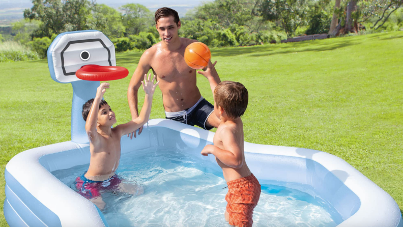 Father and two sons in child-sized pool enjoying playing basketball together outdoors.