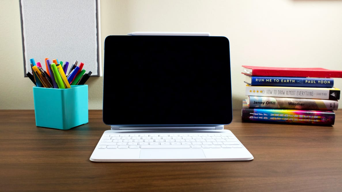 A tablet with an attached keyboard on a desk with a pencil holder and books