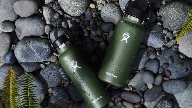 Two green Hydro Flask water bottles laying on a stone path.