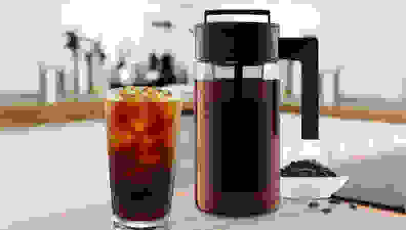 Glass of cold brew coffee next to jug-shaped cold brew maker on a kitchen counter.