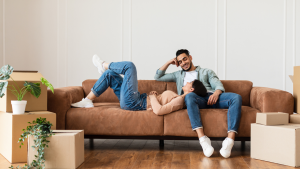 A couple lounging on a couch surrounded by moving boxes.