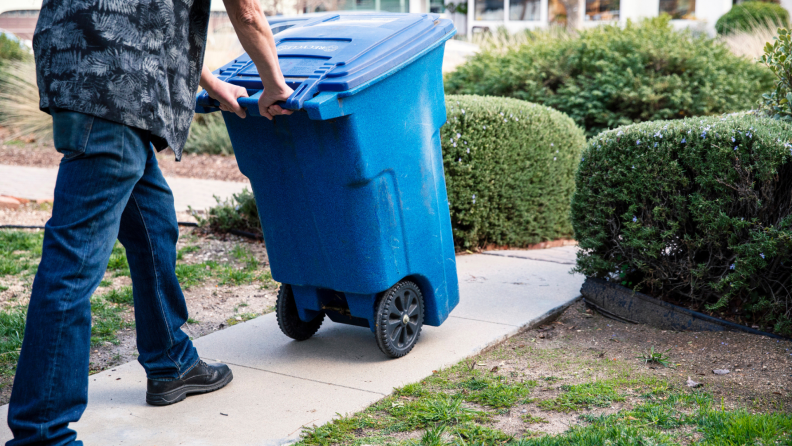 A person takes out the recycle bin to the curb.