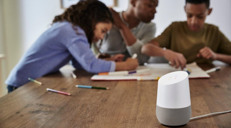 A family sits at a table with a Google Home speaker.