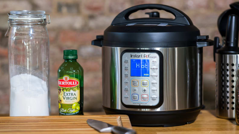 An Instant Pot on a table besides a cutting board a bottle of olive oil and a jar of flour.