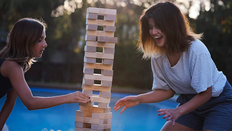 Two people play with an oversized Jenga tower outside.