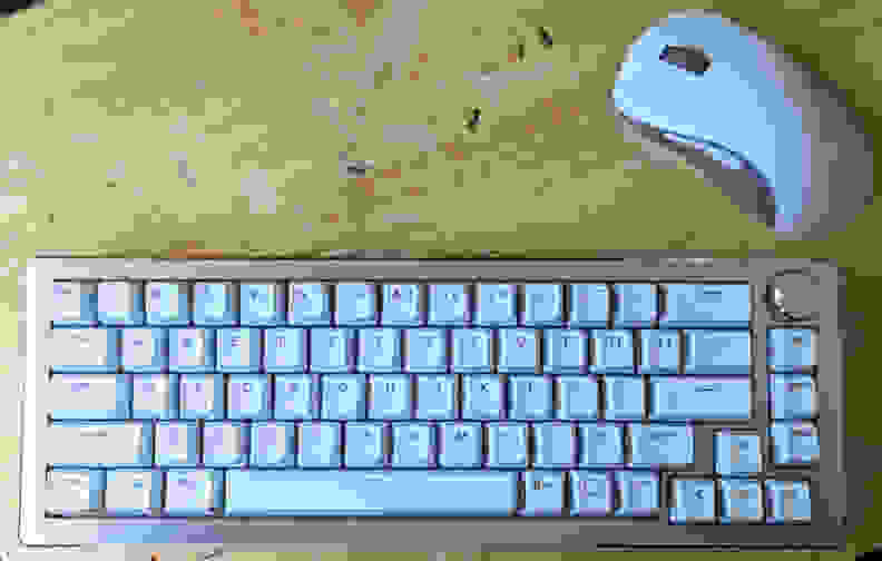 A white keyboard with a white mouse on top of a light brown desk