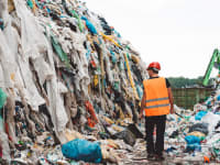 man in landfill surrounded by used clothing
