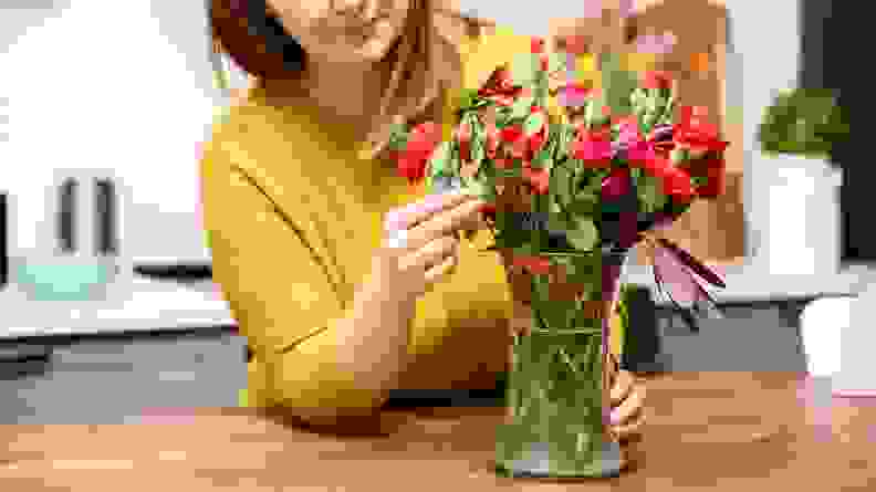 A woman admiring a bouquet of red roses sitting in a vase on a wooden countertop.