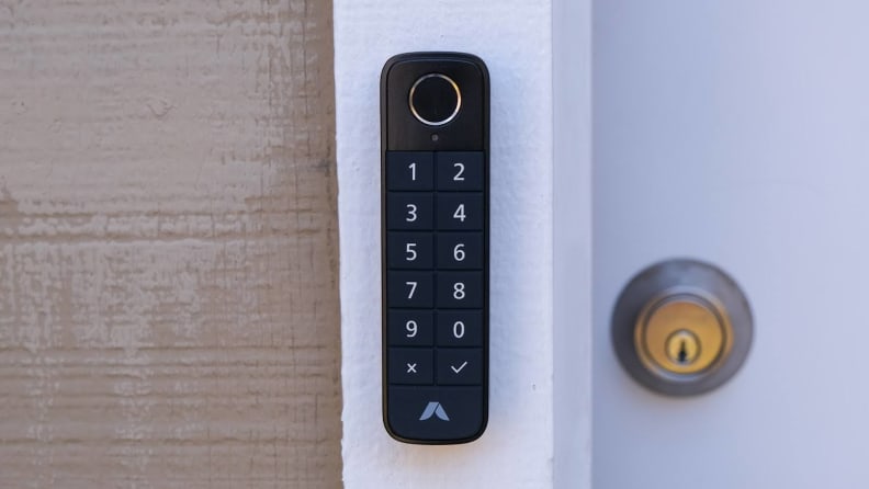 The Abode Lock Keypad mounted on a white wood door frame next to a key lock on a door.