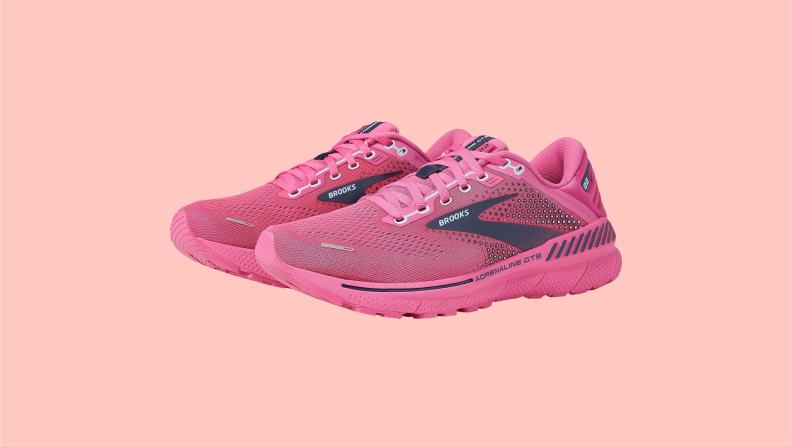 A side view of a pair of pink Brooks running shoes featuring the Brooks logo in black with white letters.