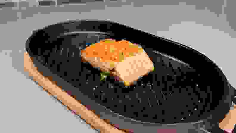 Small piece of cooked salmon on top of black grill pan.
