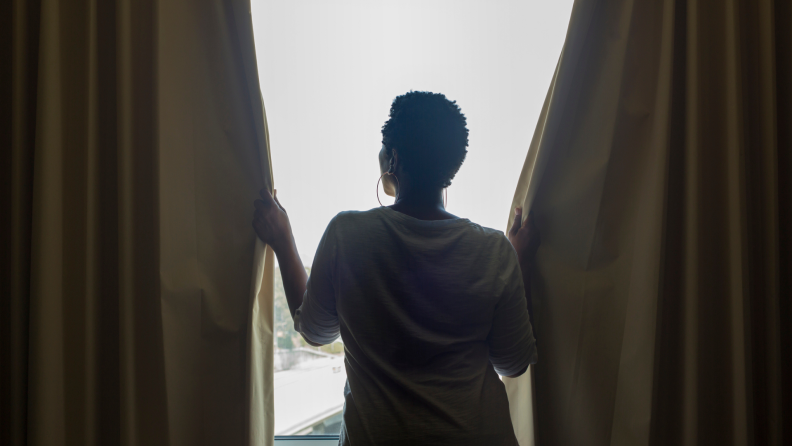 Person's silhouette opening or closing long curtains in front of a window