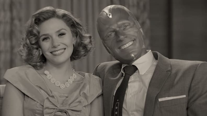 A black and white still from WandaVision featuring Wanda Maximoff and Vision on a sofa in 50s clothes.