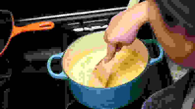 A person mixing pumpkin pie filling in a pot on a stove.