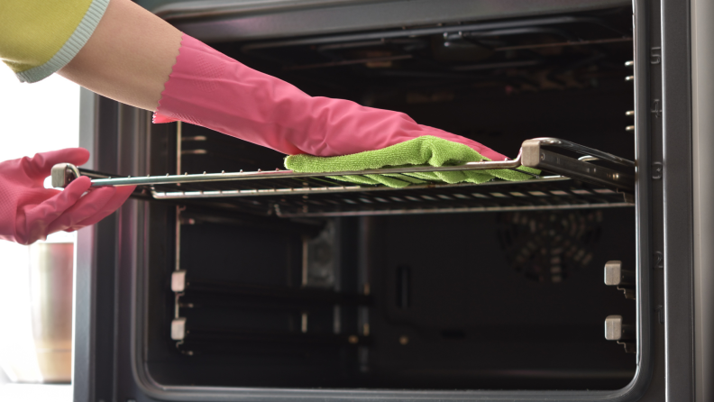 A gloved hand wiping down an oven with a microfiber cloth.