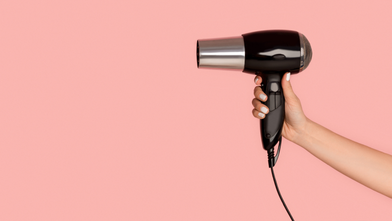 A hang holding a black blow dryer against a pink background