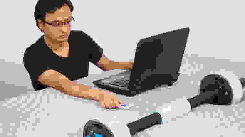 Person conducting a series of tests on the Sealy Posturepedic mattress with a weighted tool and a laptop.