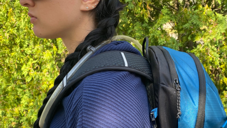 A person stands to the side as they wear the Mammut Lithium 20 Backpack outdoors.