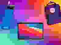 Rainbow background with a blue water bottle, Apple laptop, and small purple backpack